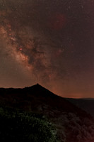 Milky way core above mountain observatory with brush illuminated in foreground