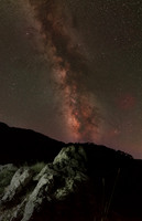 Milky way core extending vertically above rocky hillside outcrop