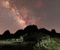 Stone shelter illuminated under mountain top and milky way core